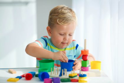 A little boy plays with wooden toys and builds a tower. Educational logic toys for children.