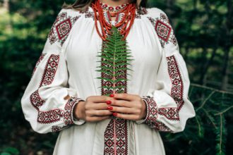 Authentic woman in traditional ukrainian costume with fern in forest.