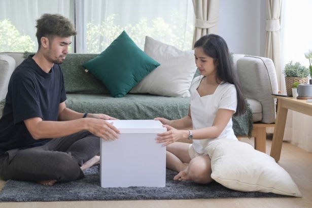 Happy young couple sitting on floor and preparing personal stuff for removal day.