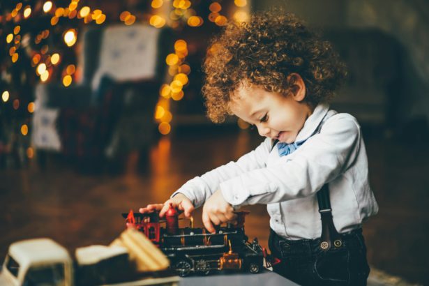 Mixed race little cute boy playing with toy train in the xmas morning.