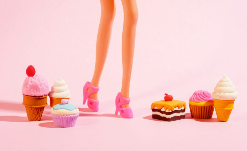 Plastic toy legs with high heels and little sweets on pastel pink background